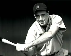 A baseball player smiles for the camera while posing with a bat, wearing a cap with a Old English "D".