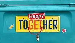 An image with a cyan background. The series title is displayed on the center of the image, above a car plate.