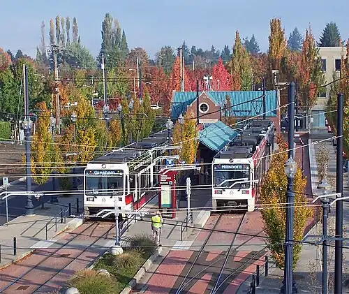 Photograph of a train station with two trains at its platforms with a road to the right