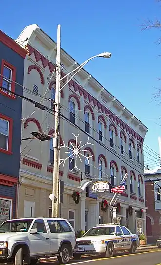 A three-story high brick building with a decorative facade mostly painted yellow photographed from its left. Two police cars and a streetlight are in front.