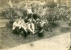 Group of well dressed women and men stting on a lawn next to a porch