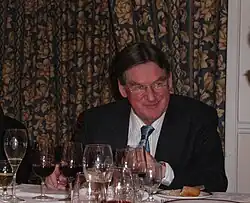 A formally dressed man sits at a table with several wine glasses on it