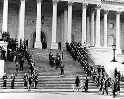 Pall bearers carrying the casket of President Kennedy up the center steps of the United States Capitol Building, followed by a color guard holding the flag of the president of the United States, and the late President's widow, Jacqueline Kennedy and her children, Caroline Kennedy and John F. Kennedy Jr., on November 24, 1963.