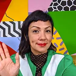 Jenifer Wofford artist bio photo 2022 standing in front of her piece with one hand raised