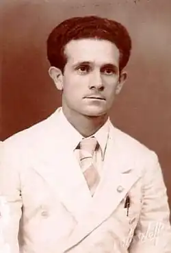 Black and white portrait of Pierats in a white suit and tie