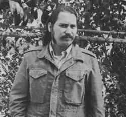 Black and white photo of Tommasi standing in front of a fence, not wearing any explicitly Nazi items