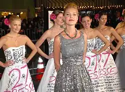 Heigl in a grey and silver dress, behind her several women wearing the same white dress from the film poster