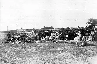Firers in the prone position and coaches, seated on chairs with telescopes, on a grass firing point: the Stickledown clock tower is just visible in the distance.