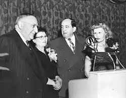 Black-and-white photograph of four people lined up near a lectern and microphone