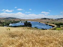 A hillside covered in dry grass overlooks a large shallow lagoon of blue water