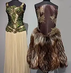 Two ensembles on mannequins. Left: Sleeveless long dress with green and gold top and white skirt. Right: Strapless short dress with brown leather top and fur skirt.