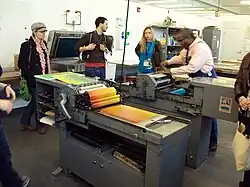 Kennedy operates a press while three people watch.