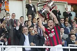 Lincoln Red Imps Captain lifting 2014 Rock Cup from Platini