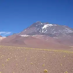 A dark tongue of lava descends from a low mountain with snowy patches