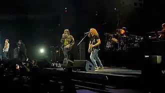 My Chemical Romance performing live. Gerard Way and Frank Iero are in the center of the image facing left, with the former singing and the latter playing an electric guitar. The other members of the band are in the background.