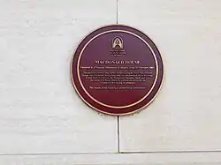 A red and gold plaque on the outside front of MacDonald House's white ground floor cladding as a national monument. It also commemorates the bombing.