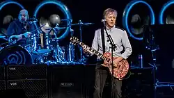McCartney holds a guitar while performing on stage.