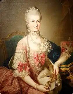 Young woman wearing an elaborate pink dress with white lace, pink ribbons, and diamond jewellery. There is a fan in her hand; she is seated before a plain background, looking directly at the viewer. Her hair is long and powdered white.