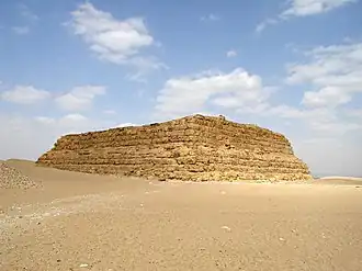A large rectangular structure of yellow mudbricks in the desert