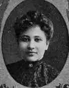 An oval yearbook photograph of a young African-American woman wearing a high-necked ruffled blouse. Her hair is in a bouffant updo.