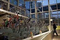 Side view of bikes parked in indoor bike racks, with tall windows beyond the racks