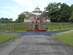 A building on a hill with stars and a fountain in front of it, with pavement leading off from it