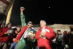 Color image of the mining leader and the Chilean President leading the rescue workers on the surface at night in a rendition of the Chilean anthem