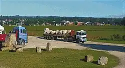 A dump truck carrying rocks from a local quarry, with the city of Batán in the background