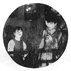 A black-and-white image, cropped in a circle, of two women looking at a caged bird