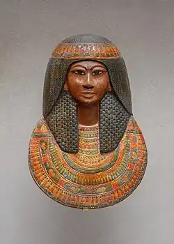 Mummy mask wearing large wig and floral collar