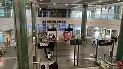Open view of the wide concourse level with pillars supporting the structure. A set of escalators ahead leads to the underground platforms.
