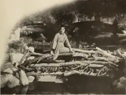 Tsuru Aoki is seated upon a log in kimono