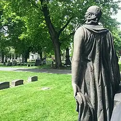 Photo showing part of a grave marker that is the sculpture of a woman and an oversight of the rest of the cemetery