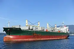 A large cargo ship is depicted. The lower hull is red, and the upper hull is green. The words Ocean Glory are printed on the side