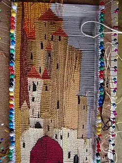 Cotton-and-silk weft-faced tapestry on pins in cork sheet; the complexity of the weft means it has to be woven manually