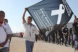 Child holding the edges of a flag with a white ribbon symbol and text regarding the White Ribbon Day march within a larger parade
