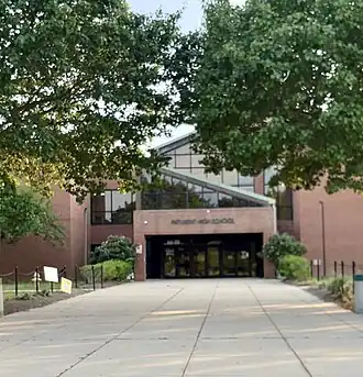Multi-story brick building with angled rooflines an entry walkway surrounded by trees