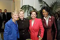 Four adult women standing in a lobby perhaps, stiff pose, large indoor plant in background