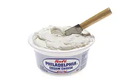 A knife stuck in a tub of cream cheese.