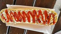 A typical zapiekanka with mushrooms under melted cheese smeared with ketchup, served on a paper tray