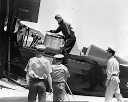 Black and white photograph of three men in khaki uniforms standing in front of a plane's centre, one man in aviator's uniform is deboarding while another person also in uniform is seated in the plane