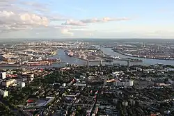 A color photograph showing an aerial view of a city. The bottom of the photograph shows more of the city's buildings and houses, while towards the center and upward is the city's waterways.