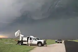 A large radar dish mounted on a white pickup truck scans the dark, cloudy sky