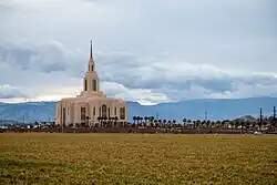 A landscape picture of the Red Cliffs temple, with a large field leading to the temple. Mountains can be seen in the distance along with rolling clouds.