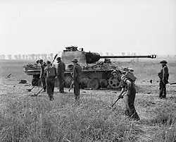 Royal Engineers sweep for mines around a destroyed German tank