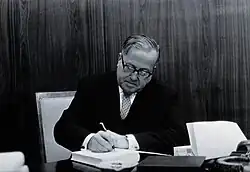 Rudolf Geigy, seated at a table, signing a book