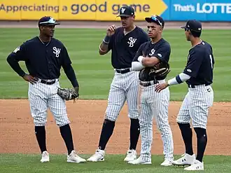 Four baseball players wearing navy blue jerseys with white pinstriped pants standing on a baseball field
