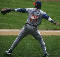 A man wearing a blue hat and gray baseball uniform bearing the number 21 prepares to throw a baseball.