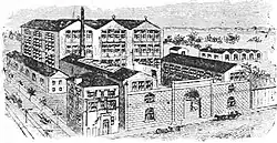 Large factory set up, showing several buildings surrounded by a high wall