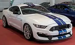 Front three-quarters view of a two-door coupe car with two blue stripes running down its roof, hood, and bumper cover